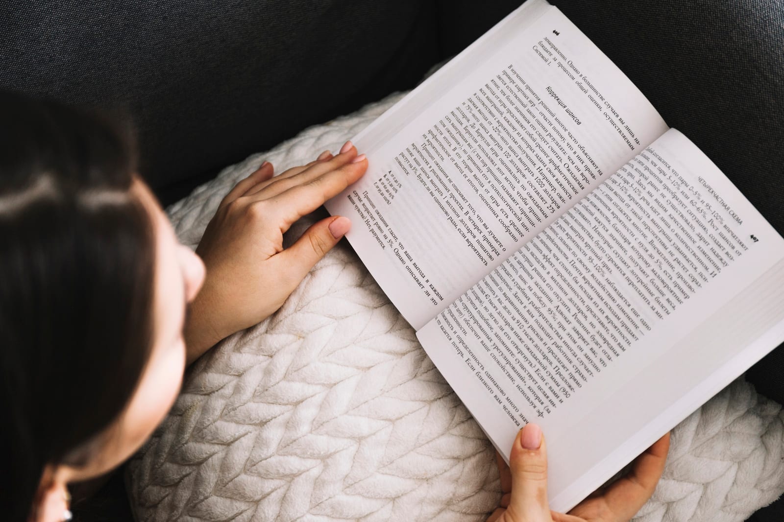 Mulher lendo um livro aberto, sentada em um sofá