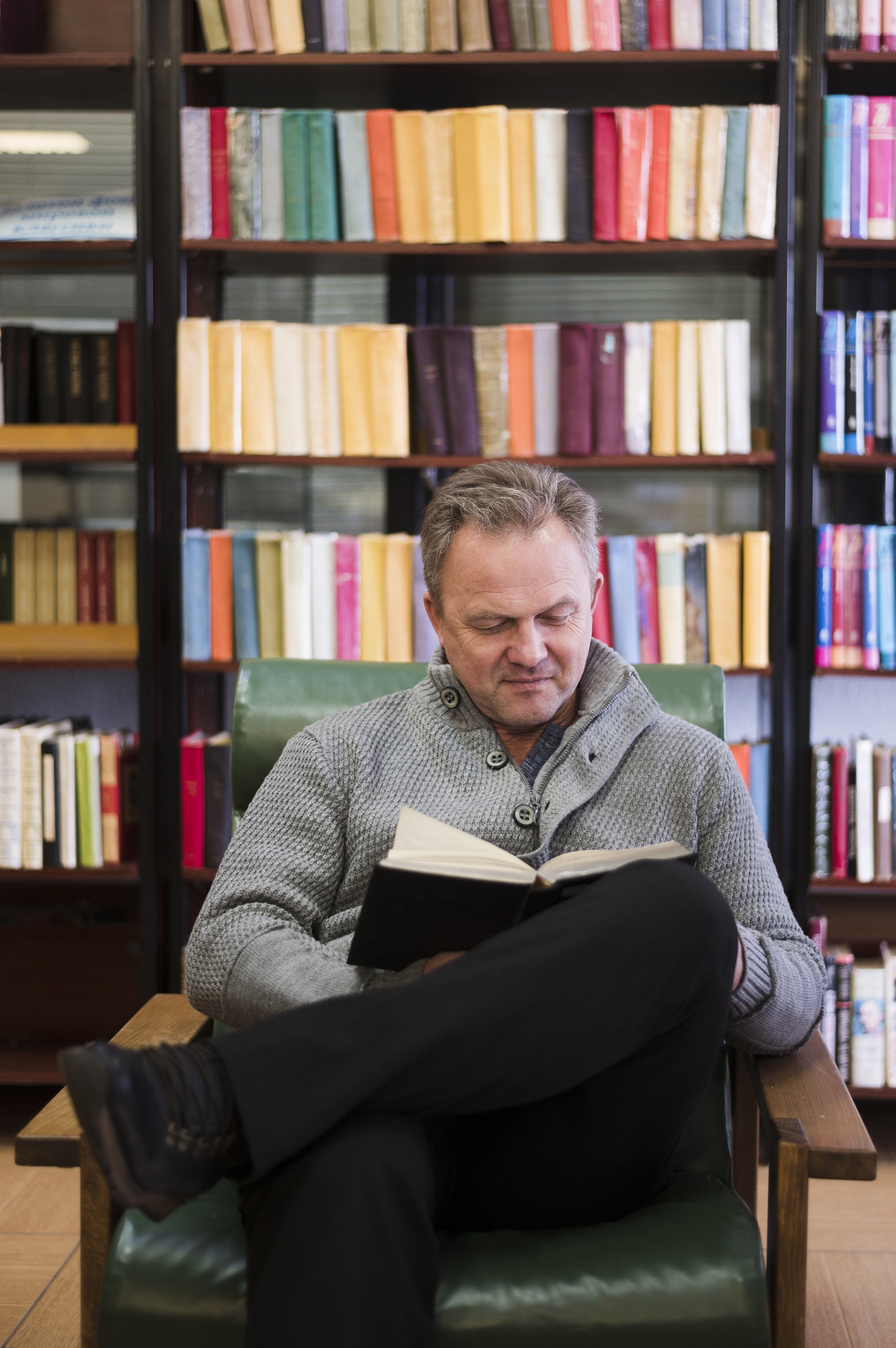 Homem lendo um livro em poltrona de couro, cercado por estantes repletas de livros